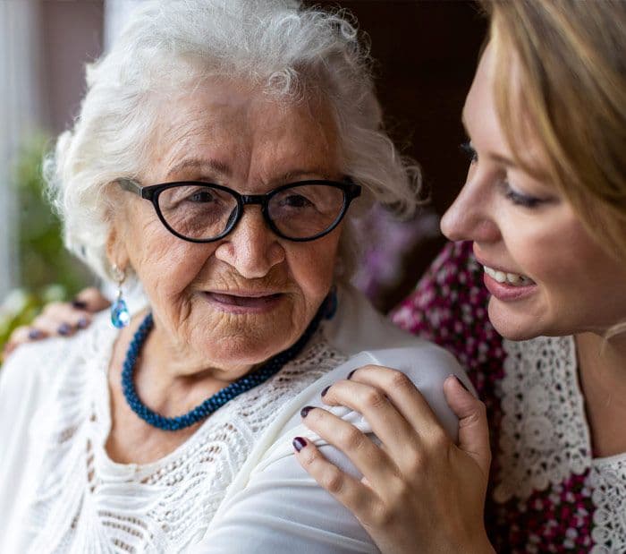 A young woman smiling with her hand on an elderly woman's shoulder